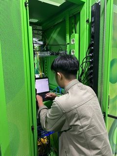 Anggota tim mengonfigurasi perangkat jaringan dari laptop di depan rak server yang terbuka.